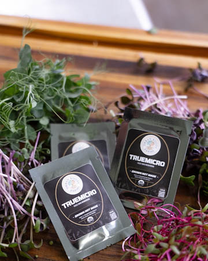 TrueMicro single-serve travel packets on a wood bench with fresh microgreens
